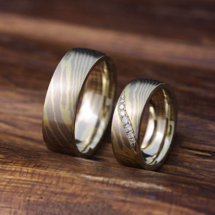 Mokume Gane - Trauringe mit mittelstarker Tordierung - In japanischer Schmiedetechnik fugenlos gefertigte Eheringe aus Palladium und Grüngold. Der Struktur folgend sind sieben hochwertige Diamanten in Pavé-Verschnitt eingefasst.