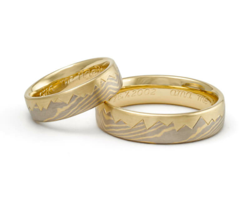 Luxuriöse Mokume Gane Eheringe mit Bergpanorama und fließender Maserung aus Gelbgold und Graugold.